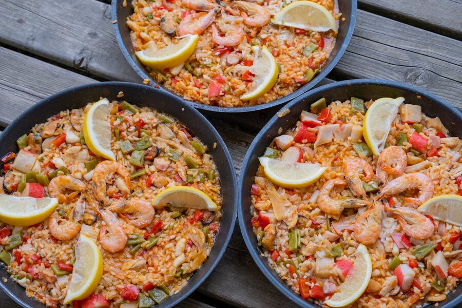 Three pans of paella with fresh lemon slices on a rustic wooden table