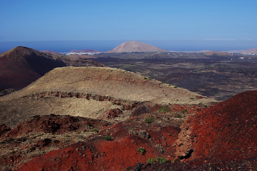 Red volcanic crater formation in Timanfaya with Atlantic coast in background