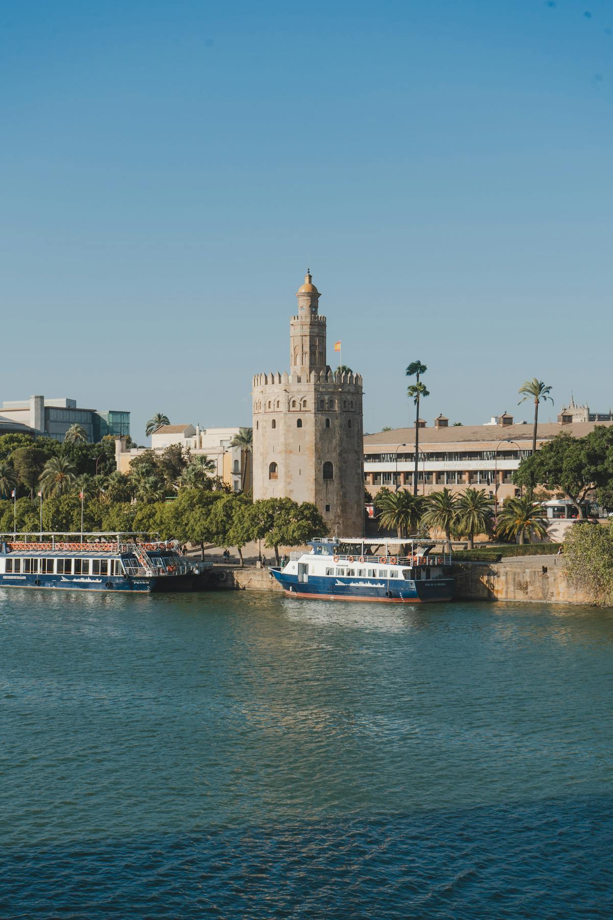 The Torre del Oro tower beside the Guadalquivir River with tour boats docked in Seville