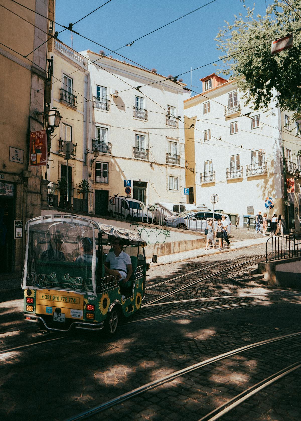 Tuk-tuk driving alongside tram tracks in a sunlit Lisbon street