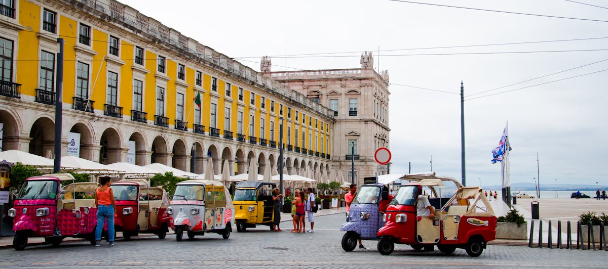 Row of colorful tuk-tuks parked in a Lisbon square with historic buildings behind them