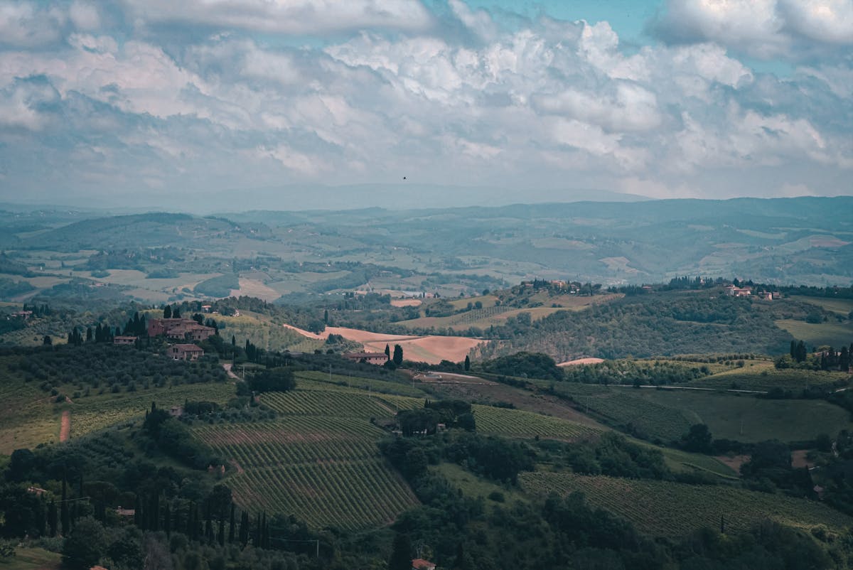 Wide panoramic view of rolling Tuscan countryside with scattered farmhouses and cypress trees