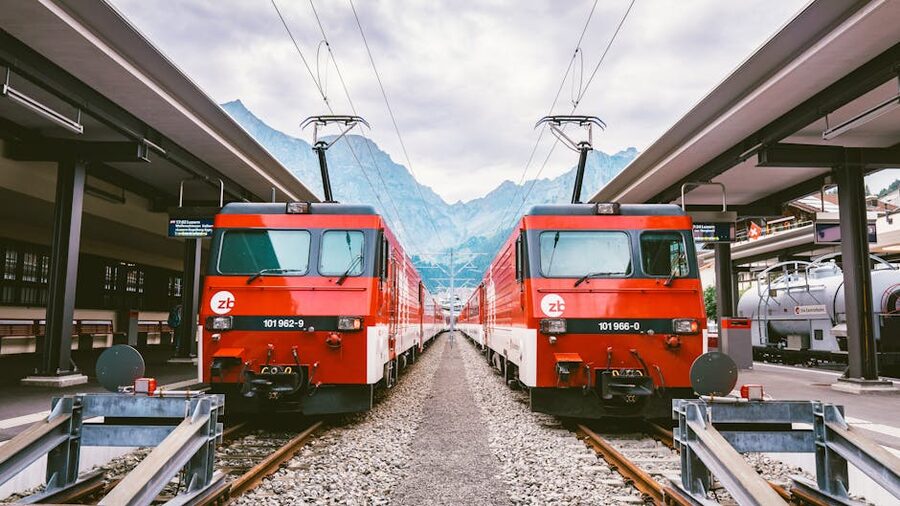 Two red Swiss trains at station with mountains