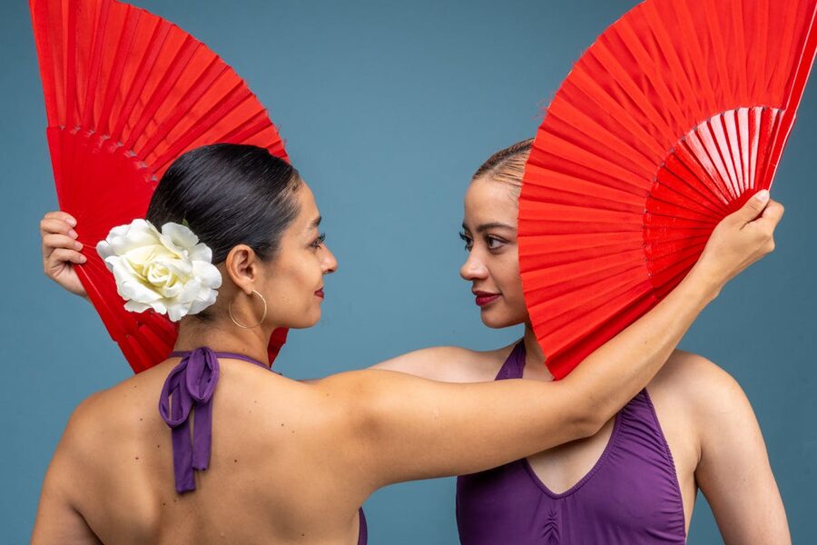Two women holding red fans in a studio flamenco setting