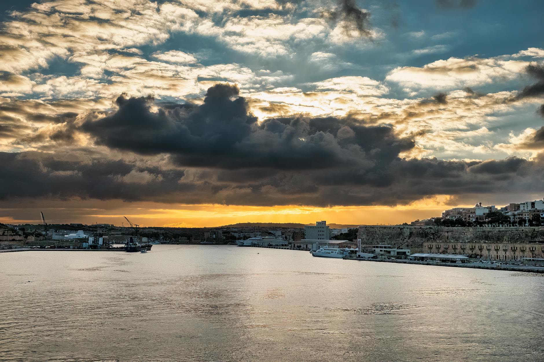 Dramatic sunset over Valletta harbour with clouds reflected in the water
