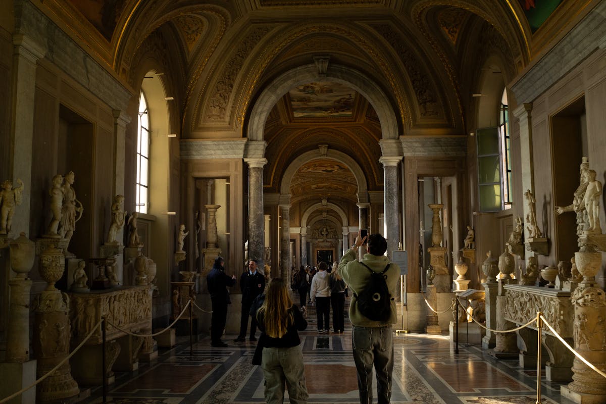 Ancient marble sculptures in a grand hallway of the Vatican Museums with visitors
