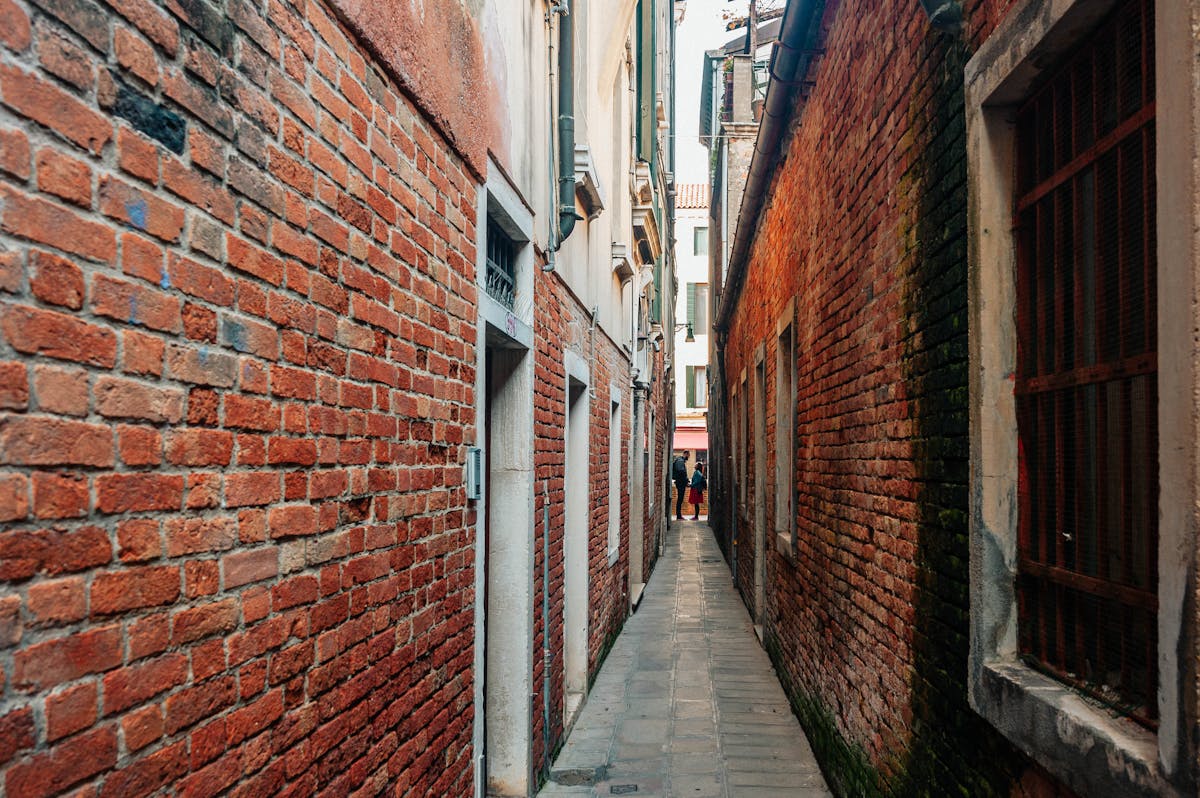 Narrow brick alleyway in Venice leading to a distant canal