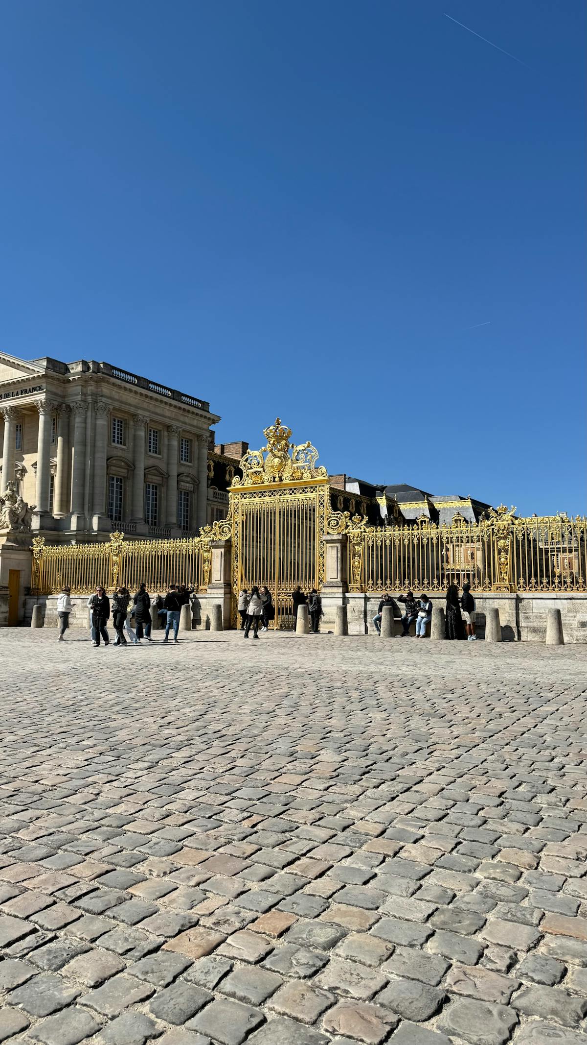 Visitors gathering at the ornate golden entrance gates of the Palace of Versailles