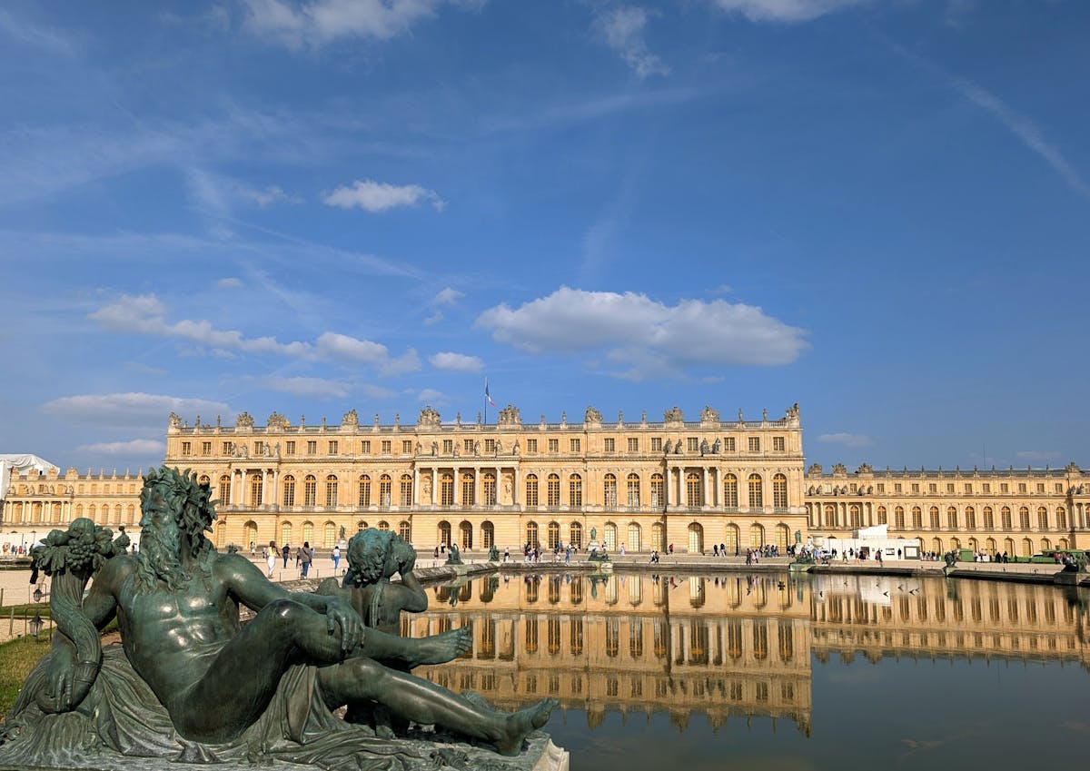 The Palace of Versailles reflected in the water of the gardens under a blue sky