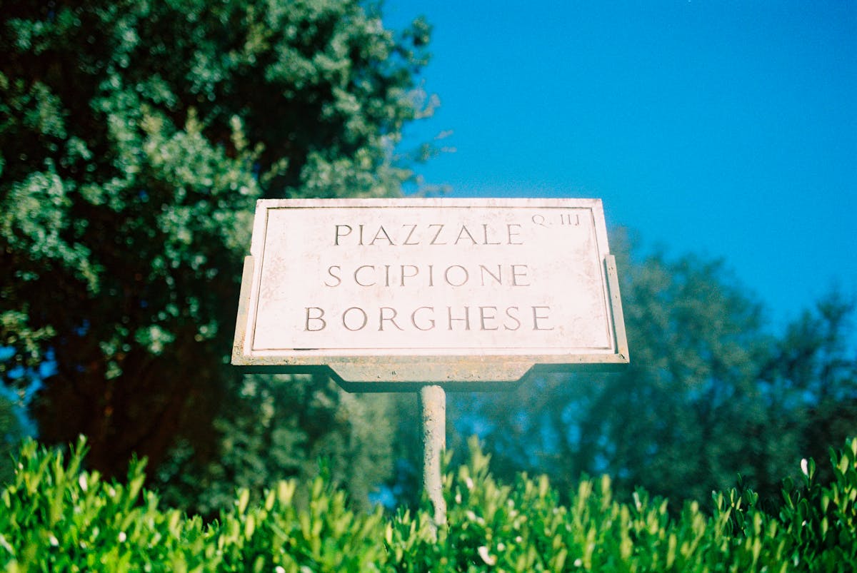 Vintage green sign reading Piazzale Scipione Borghese surrounded by greenery in the Villa Borghese park in Rome
