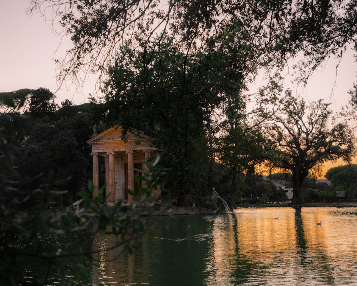 The Temple of Aesculapius reflecting in a pond at sunset in the Villa Borghese Gardens in Rome