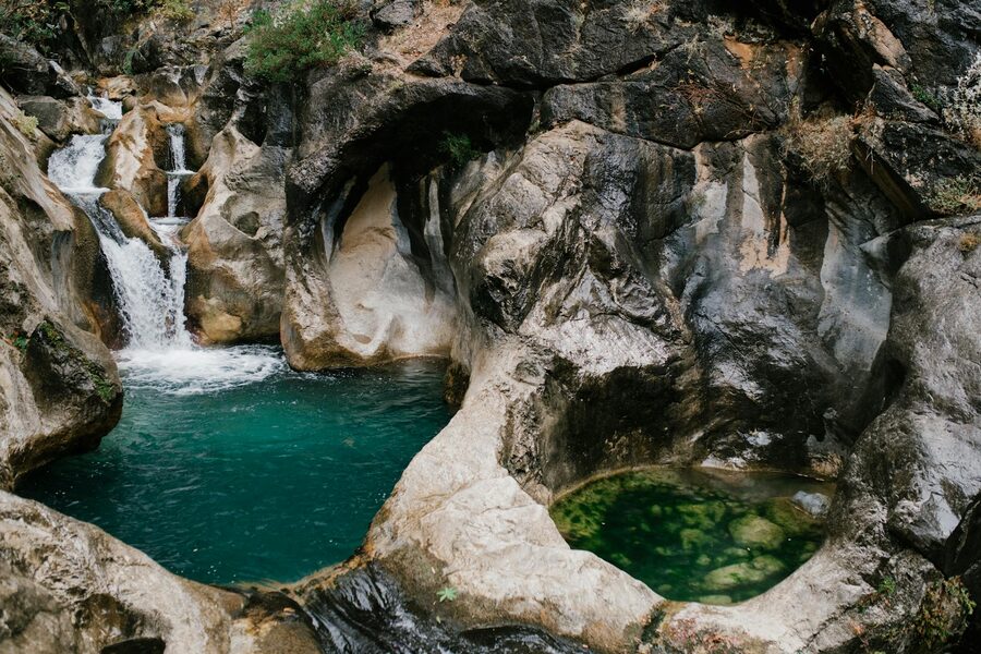 Waterfall flowing over rocks into a canyon stream surrounded by greenery
