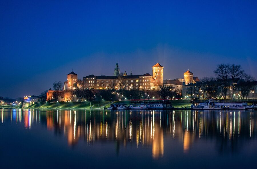 Wawel Castle illuminated with river boats moored below in Krakow