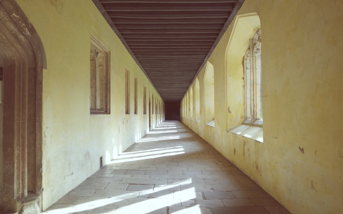 Gothic cloister corridor with arched windows casting shadows on stone floor