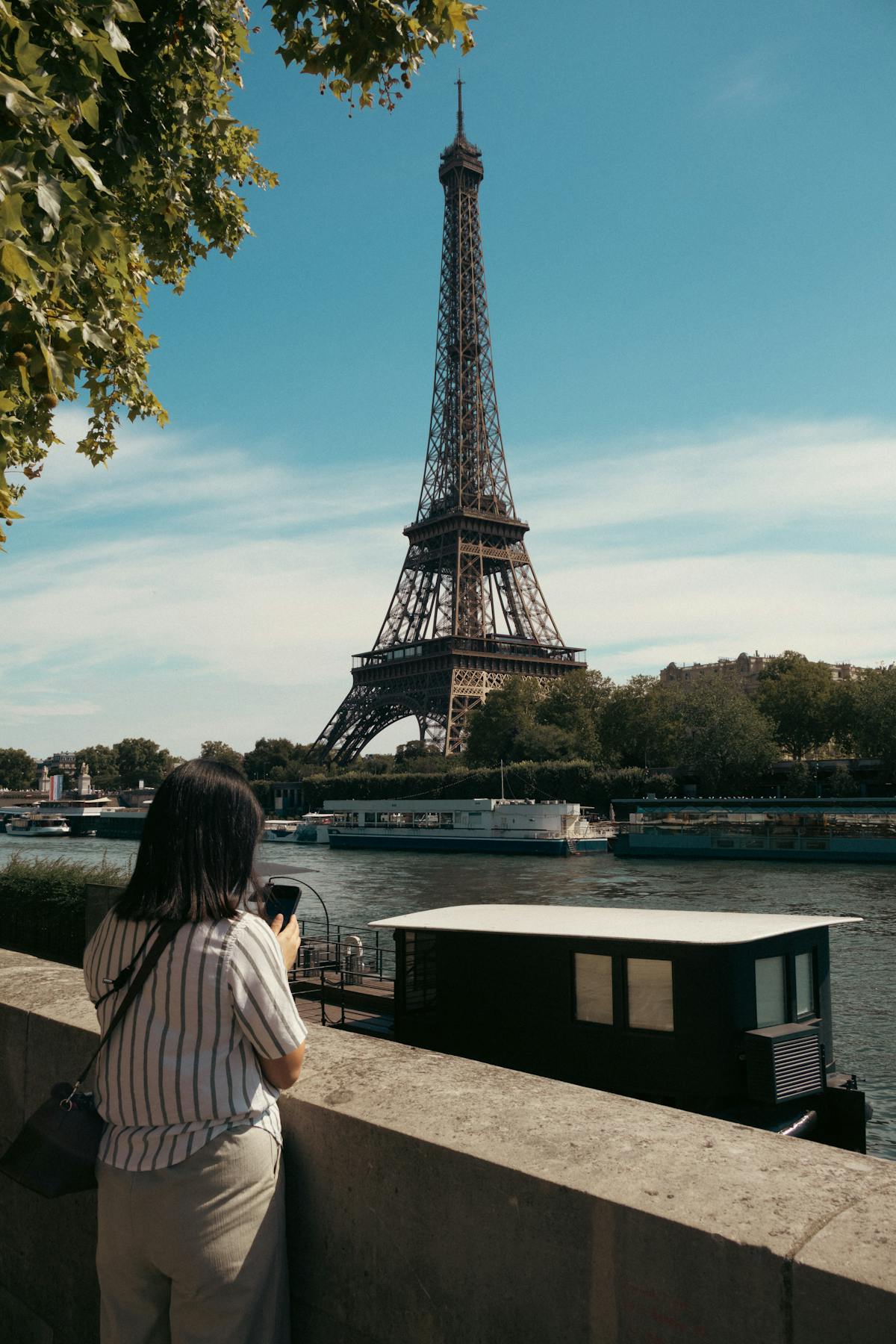 A woman admires the Eiffel Tower from across the Seine on a sunny day