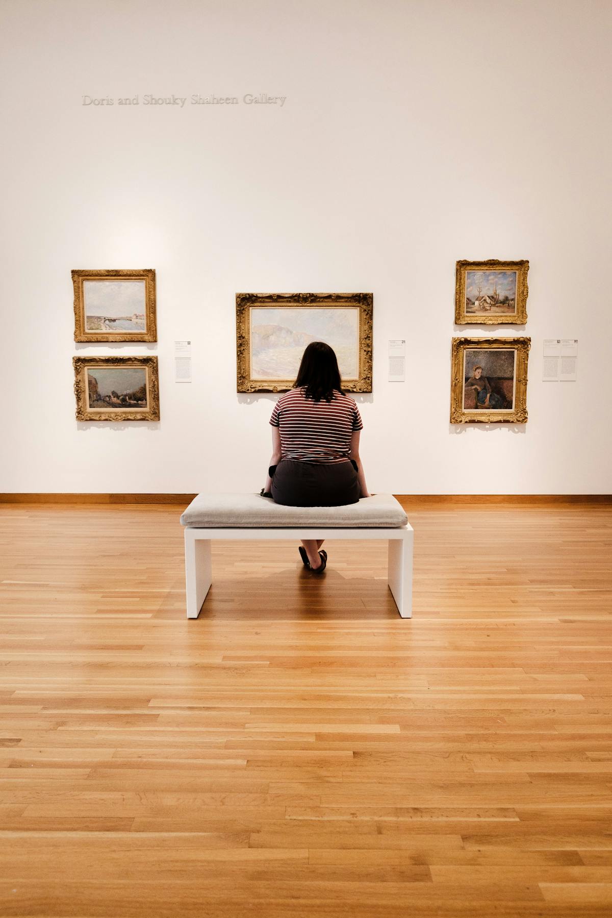 A woman sitting in an art museum admiring paintings in a serene contemplative atmosphere