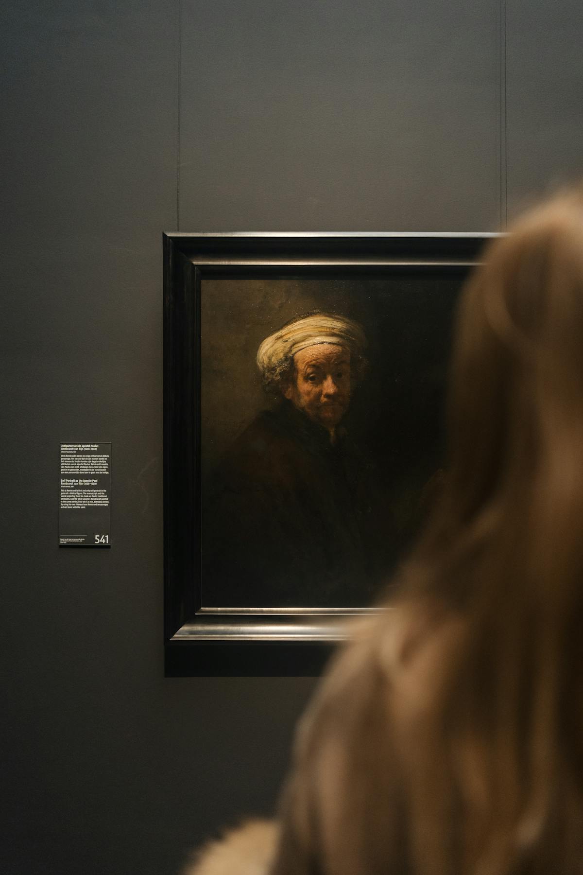 A woman with long hair studying a Renaissance painting in the Rijksmuseum gallery