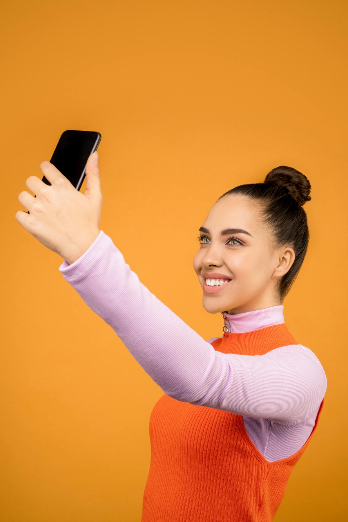 Smiling woman taking selfie with phone on orange background