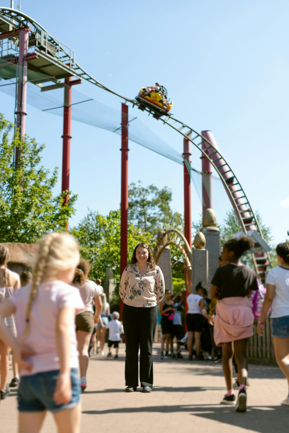 Woman enjoying a sunny day at a theme park with a roller coaster overhead
