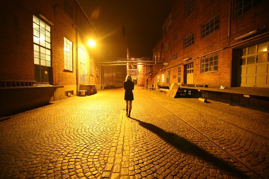 Woman walking down lit cobblestone alley