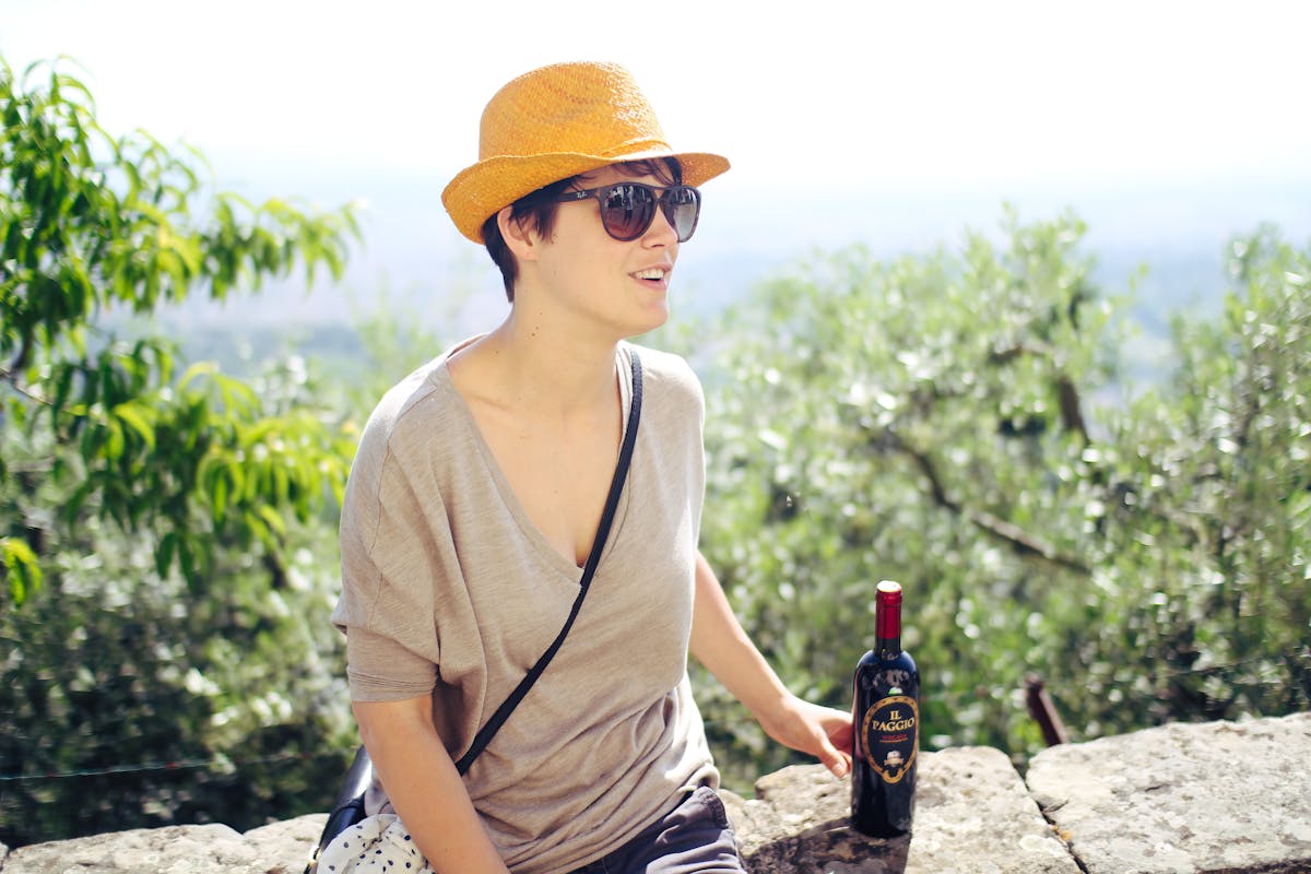 A woman wearing a yellow hat enjoying a glass of wine outdoors in the Tuscan countryside