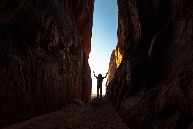 Silhouette of an explorer standing inside a deep canyon gorge looking up at the sky