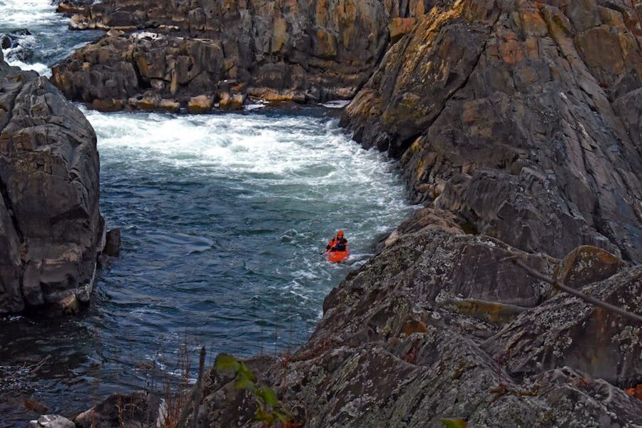Kayaker in river rapids over rocks