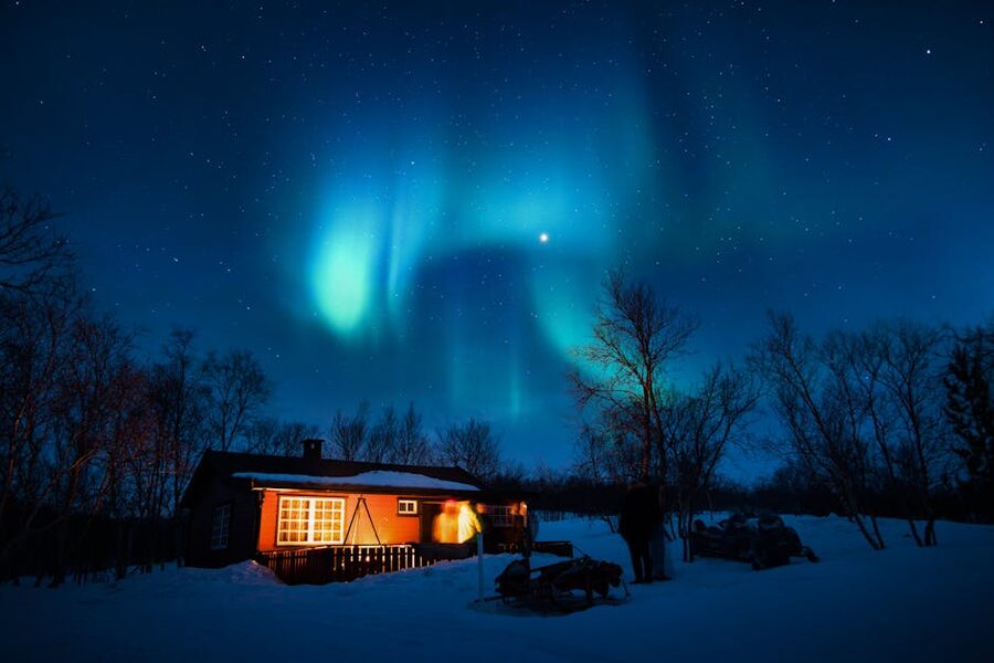 Lit cabin under aurora and stars