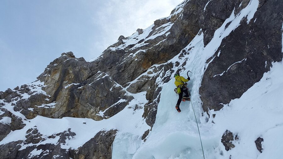 Climber on a steep blue icefall in alpine setting