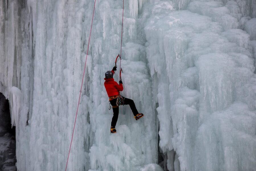 Ice climber in a red shell jacket on a frozen wall