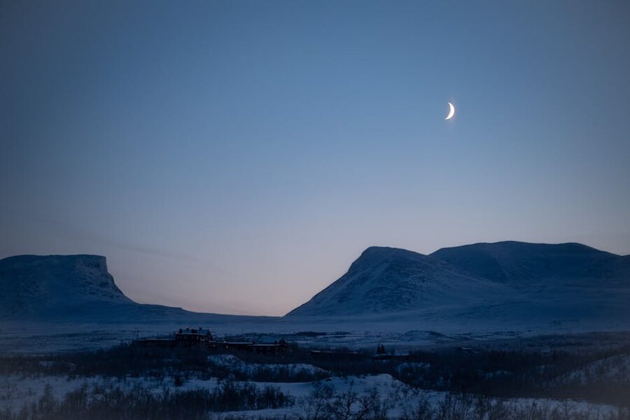 Winter twilight over Abisko with crescent moon and snowy peaks