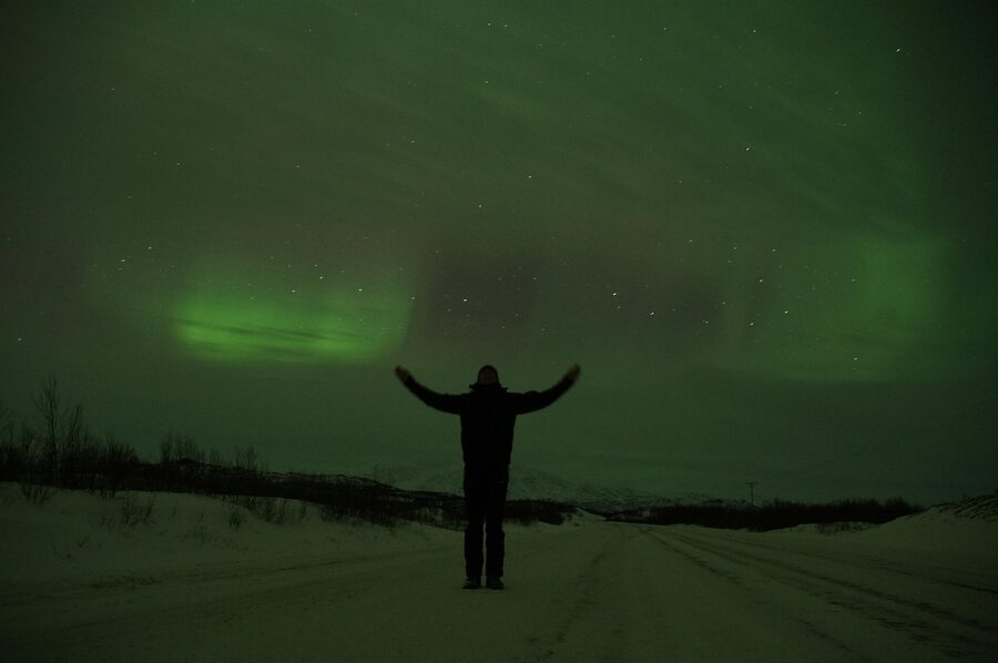 Empty snow road under aurora in Swedish Lapland