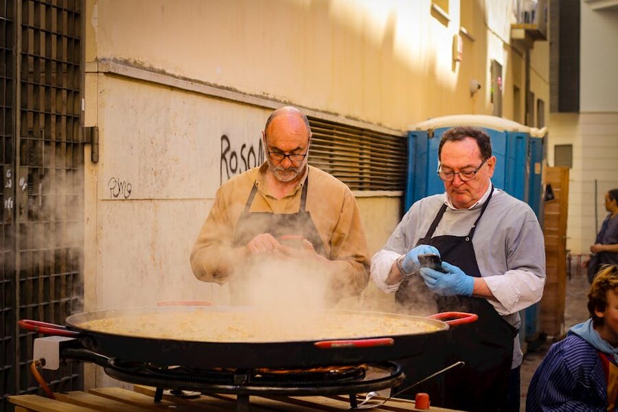 Two chefs cooking a large paella outdoors