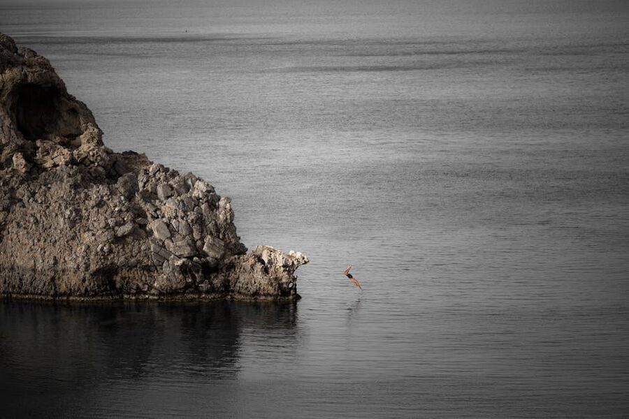 A diver mid-air after jumping off a rocky cliff into the sea