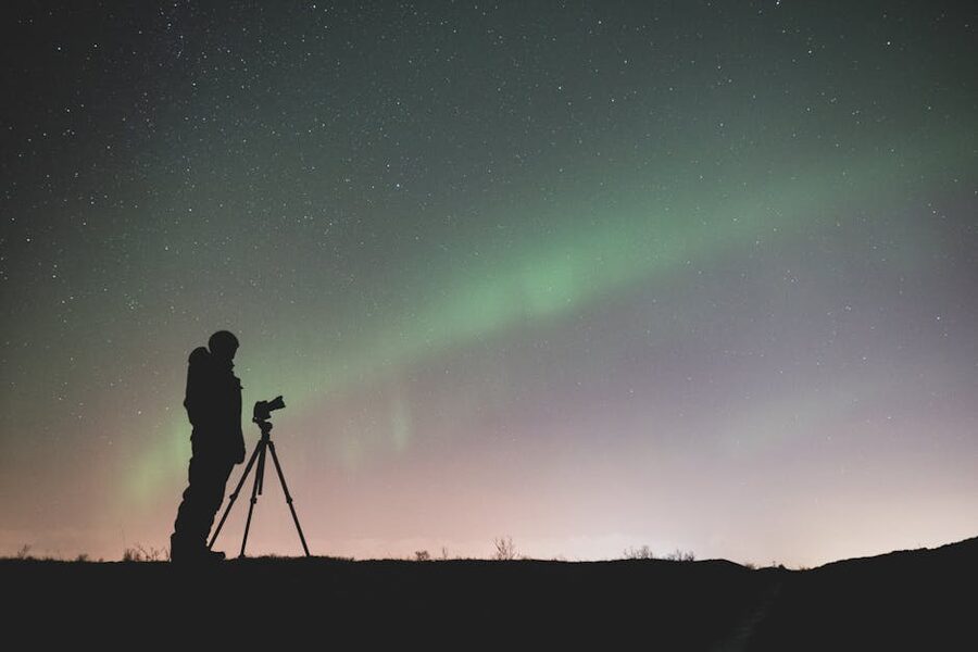 Silhouette of a photographer with tripod under green northern lights