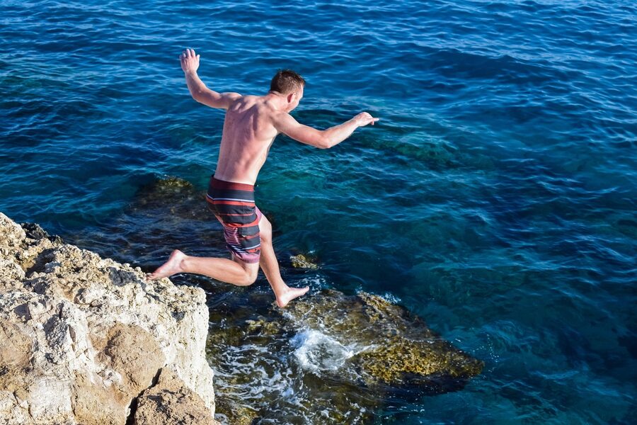 Cliff jumper leaping from a rocky ledge into blue sea
