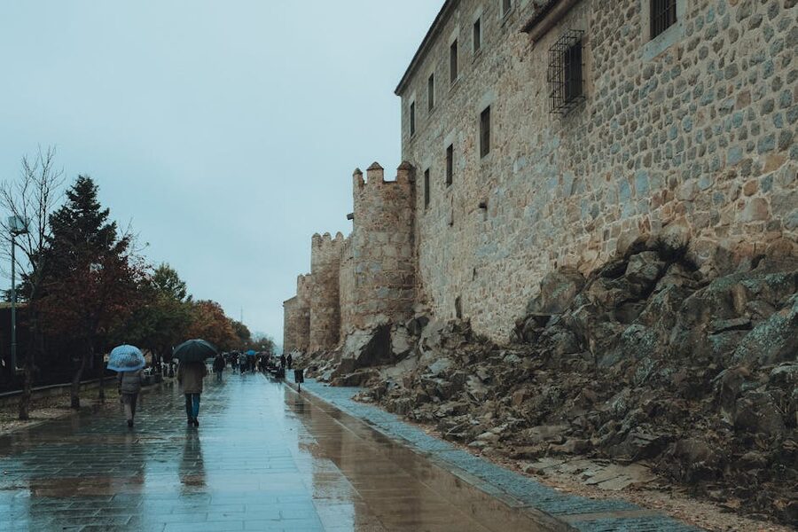 People walking by Avila walls on a rainy day