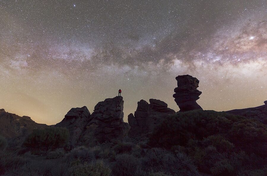 Long exposure of the Milky Way above Roques de Garcia in Teide National Park with a person standing on the rocks
