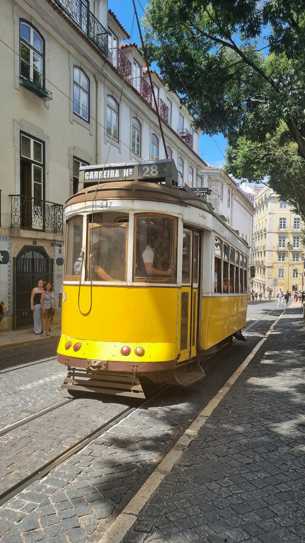 Iconic yellow tram navigating a street in Lisbon on a sunny day